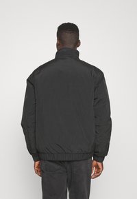 Giacca a vento nera con collo alto, polsini elastici e orlo corto. Texture liscia con un design leggero.