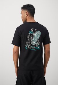 Black cotton t-shirt featuring a colorful graphic on the back of a figure with a mountain backdrop and "The North Face" text at the center.