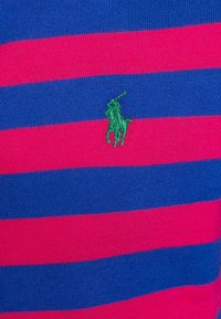 Randig pikétröja med breda horisontella band i ljusrosa och djupblå bomull. Broderad grön logotyp med en häst och ryttare på bröstet.