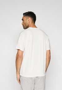 T-shirt de algodão branco com mangas curtas, corte descontraído, gola redonda e textura suave, vista de costas contra um fundo simples.