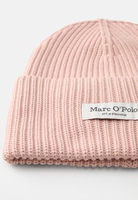Gorro de malha rosa claro com textura canelada, com a aba dobrada, e uma etiqueta branca com "Marc O'Polo" e "EST. EM ESTOCOLMO."