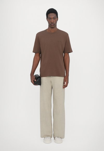 Brown short-sleeve t-shirt with a crew neck, paired with light beige wide-leg trousers. The model holds a black textured clutch bag.
