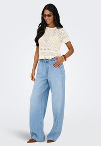 Haut crème en maille crochet à manches courtes associé à un pantalon en denim bleu clair ample et des ballerines pointues marron. Accessoirisé avec un bracelet.