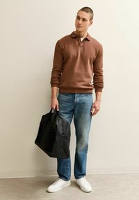 Braunes Langarm-Polohemd, hellblaue Jeans, schwarze Tragetasche und weiße Sneaker. Glatter Stoff, lockere Passform, minimalistisches Design.