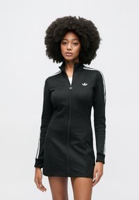 Fekete, cipzáras ruha sima anyagból, fehér oldalsávokkal és kis logóval a mellrészen. Hosszú ujjú, testhez simuló szabás.