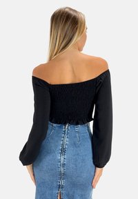 Schwarzes Off-Shoulder-Top mit strukturiertem Smocking und Glockenärmeln, kombiniert mit einem hochtaillierten blauen Jeansrock mit einem Reißverschluss hinten und einem Schlitz.