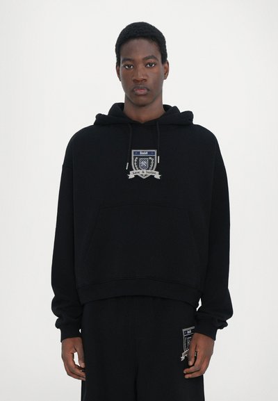 Czarna hoodie z przednią kieszenią, haftowany herb z napisem "GmbH" i "Miłość & Sprawiedliwość". Miękki materiał, luźny krój, ściągacze przy mankietach.