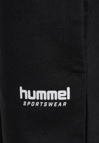 Svart sportklädesmaterial med en vit "hummel SPORTSWEAR"-logotyp. Slät textur med ribbad detalj. Inga synliga mönster eller accenter.