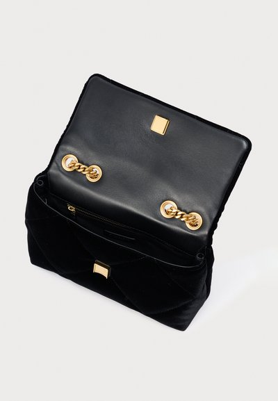 Mala de veludo preta com design acolchoado, ferragens douradas e compartimento com fecho éclair. O interior apresenta um forro preto liso.