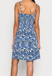 Blaues Kleid mit floralem Druck, geschmücktem Rücken, dünnen Trägern und einem ausgestellten Rock. Es zeigt eine Mischung aus dunkelblauen, hellblauen und weißen Blumen.