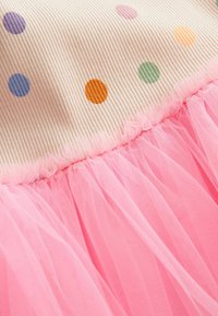 Jupe en tulle rose attachée à un tissu rayé avec des pois colorés en tons orange, vert, violet et bleu.