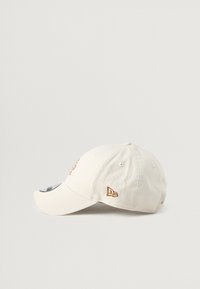 Krem bela kapica iz bombaža s vezenim logotipom v rjavi barvi, ukrivljenim obodom in prezračevalnimi luknjami na straneh. Subtilna teksturirana tkanina.