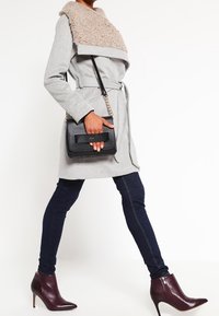 Cappotto grigio con colletto beige testurizzato, vita con cintura; abbinato a jeans skinny scuri e stivaletti borgogna. Borsa nera con dettaglio a fiocco.