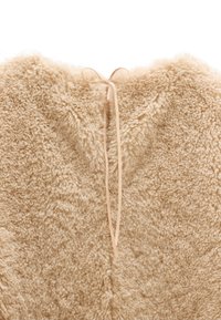 Beżowa tkanina teksturowana z puszystą, miękką powierzchnią. Posiada związaną wstążkę z tyłu, tworzącą zaokrąglony dekolt.