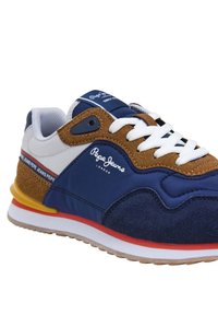 Chaussure de sport bleu marine avec des accents en suède marron, des lacets blancs et une bande rouge. Caractéristiques d'une semelle texturée et d'un marquage "Pepe Jeans London".
