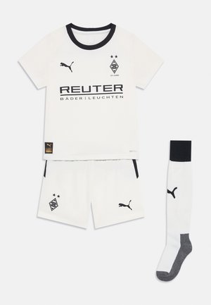Equipación de fútbol blanca con una camiseta de cuello negro que incluye un logo y texto, pantalones cortos a juego y un calcetín blanco con detalles negros.