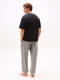 T-shirt noir à manches courtes associé à un pantalon léger gris clair, ajusté et avec des poches et des poignets froncés. Le modèle est vu de dos, pieds nus.