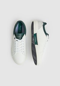 Baskets en cuir blanc avec des accents verts, design à lacets, semelle texturée et un onglet de talon gris. Présente un logo sur la languette et sur le côté.