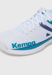 Scarpa da ginnastica bianca con tomaia in rete, accenti blu e viola, con logo "Kempa", lacci piatti e un design della suola elegante e arrotondata.