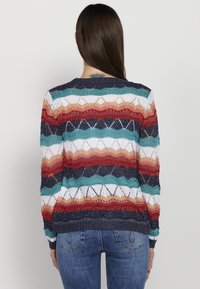 Sweter kardigan z falistym wzorem w kolorze czerwonym, teal, białym i granatowym. Posiada okrągły dekolt oraz ściągacze na końcach rękawów, prezentując otwartą teksturę splotu.
