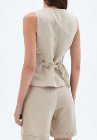 Beige ärmlös topp i texturerat tyg, med bältesdetalj bak och figursydd silhuett, kombinerad med matchande shorts.