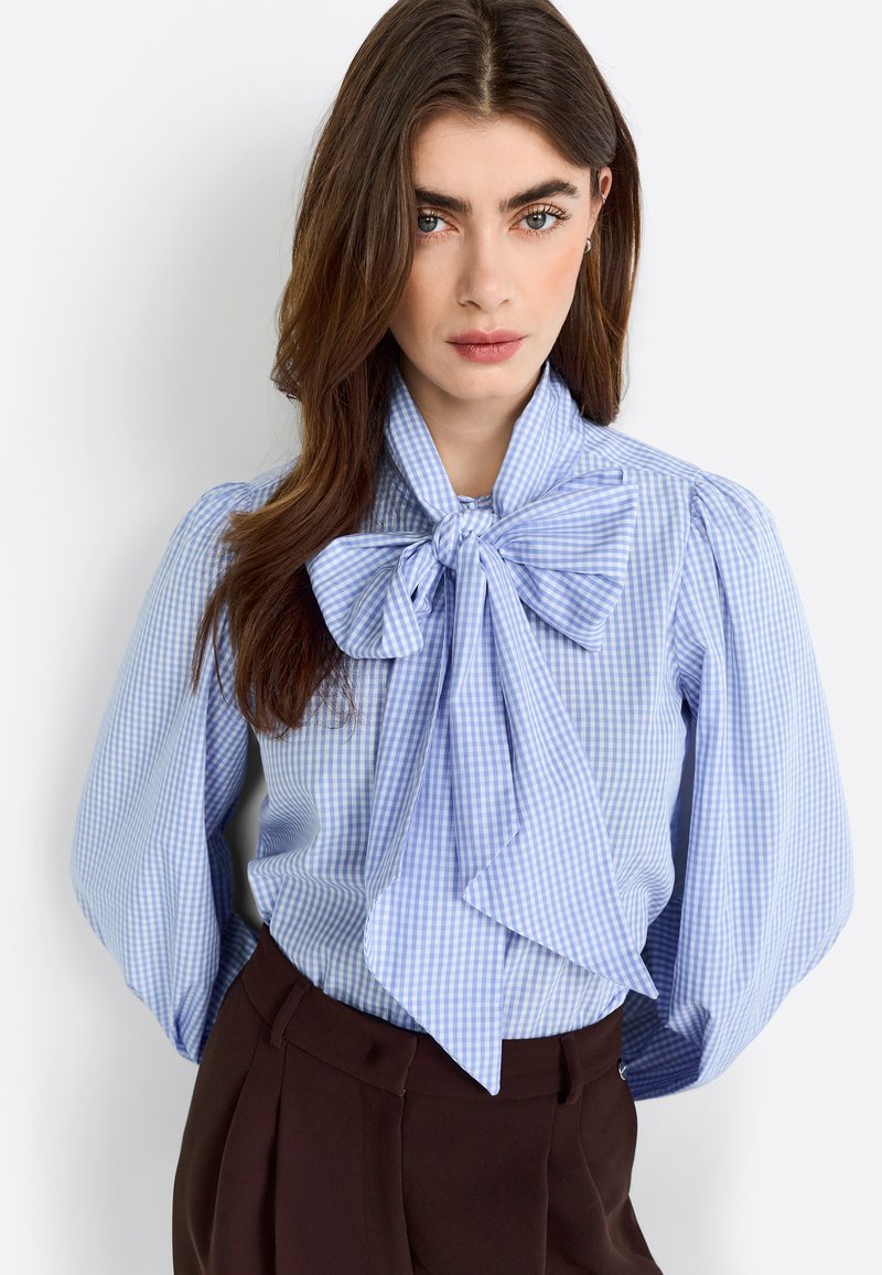 Helleblaues und weiß karriertes Bluse mit einem großen Schleifenkragen und Puffärmeln. Der Stoff wirkt glatt und hat ein poliertes Design.