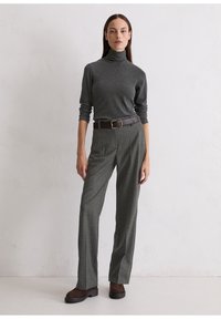 Dunkelgrauer Rollkragenpullover, kombiniert mit grauen Karohosen und einem braunen Gürtel. Braune Plateauschnürstiefel mit strukturierter Oberfläche.