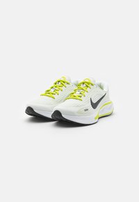 Bílé sportovní boty s texturovaným síťovaným svrškem, jasně žlutými tkaničkami a černým logem swoosh, s polstrovanou podrážkou a černou gumovou vnější podrážkou.