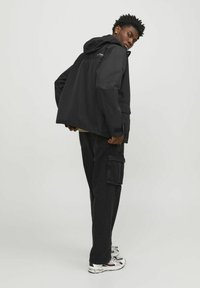 Black hooded jacket with a relaxed fit, featuring zippered pockets and a smooth texture, paired with black cargo pants and sneakers.