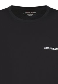 T-shirt en coton noir avec un col rond et des manches courtes ; présente un logo blanc "GUESS JEANS" sur la partie gauche de la poitrine. Texture lisse.