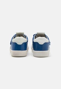 Adidași din piele albastră cu accente albe, vârf rotunjit, talpă exterioară din cauciuc alb texturat și guler moale și căptușit. Vedere din spate care evidențiază detaliile designului.