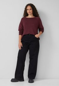 Maronenrot gestreifter Pullover mit rundem Ausschnitt und herunterhängenden Schultern, kombiniert mit hoch taillierten schwarzen, weitem Hosen und schwarzen klobigen Stiefeln.