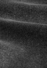 Gros plan d’un tissu gris foncé avec une texture tissée visible et des plis formant des lignes douces et courbes à travers la surface.