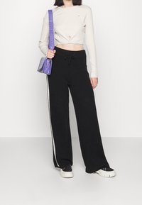 Svarta vida sweatpants med dragsko i midjan, tillsammans med en ljusbeige ribbad långärmad topp och en liten lila handväska.