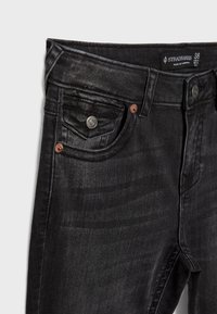 Črne jeans hlače iz denima s klasičnim pet-pocket oblikovanjem, sprednjimi zakovicami in subtilnim sijajem. Pas je označen z blagovno znamko in velikostjo.