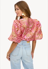 Blouse rose et dorée à motifs avec des manches bouffantes, en tissu texturé, et une coupe décontractée, associée à un jean taille haute bleu clair.