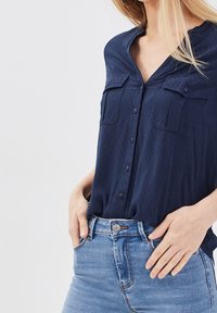 Chemise bleu marine à boutons avec un motif texturé, dotée de deux poches poitrine, associée à un jean en denim bleu clair.