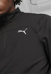 Schwarzes sportliches Quarter-Zip-Oberteil aus glattem Material. Verfügt über ein kleines reflektierendes Puma-Logo auf der linken Brust und flache Nähte.