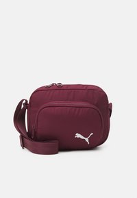 Bordeaux nylontasker til at bære på tværs med en frontlynlås, justerbar rem og hvidt Puma-logo. Glat tekstur og rektangulær form.