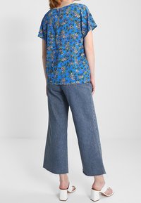 Modrý květinový top s krátkými volánkovými rukávy, spárovaný s vysokým pasem a světlými širokými džíny. Bílá sandály na blokovém podpatku dokončují vzhled.