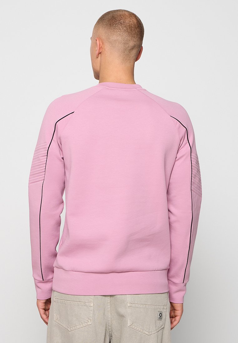 Sweatshirt rose avec un col ras du cou, des manches raglan et des détails texturés sur les épaules. Coutil noir le long des coutures. Texture de tissu douce.