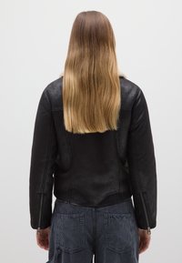 Giacca in pelle nera con finitura testurizzata, caratterizzata da un morbido colletto in pelliccia, polsini con cerniera e una silhouette aderente.