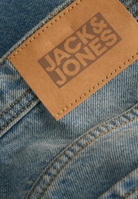 Pruun nahast tükk, millele on tikkitud "JACK & JONES" logo sinise teksariide peal.