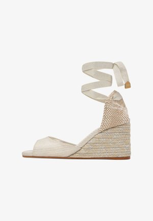 Sandalia de cuña beige con tacón trenzado, puntera abierta y larga correa envolvente para el tobillo en tejido texturizado.