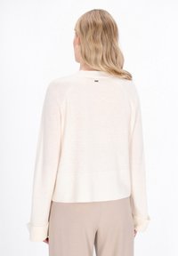 Jasno beżowy sweter wykonany z miękkiego materiału, z prążkowanym wykończeniem u dołu i na mankietach. Z tyłu znajduje się mały akcent z logo w okolicy dekoltu.