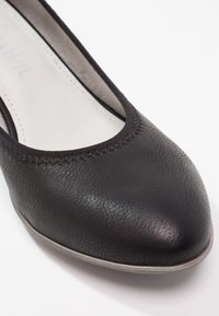 Ballerine plate en cuir noir avec bout arrondi et bordure cousue, montrant la doublure intérieure et le bord de la semelle gris clair.