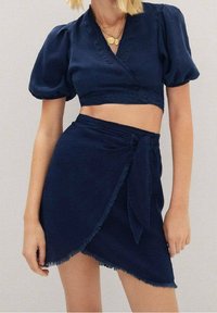 Sæt i mørkeblå bestående af en kort crop top med pufærmer og omslagsdesign samt en matchende højtaljet nederdel med bindebånd.