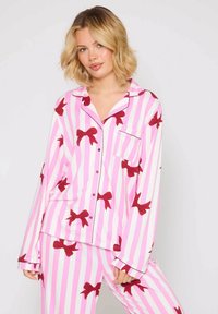 Conjunto de pijama de rayas rosas y blancas con patrones de lazos rojos. Presenta una camisa con botones y un bolsillo en el pecho, junto con pantalones de corte relajado. Tejido suave.