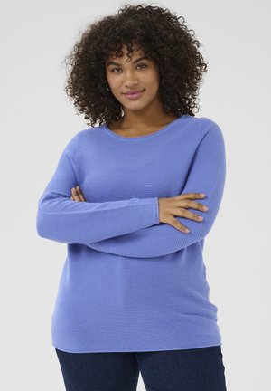 Lichtpaarse geribbelde gebreide trui met lange mouwen en een ronde halslijn, met een ontspannen pasvorm en een soepele textuur. Gecombineerd met donkerblauwe jeans.
