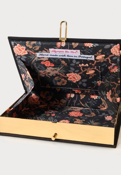 Pochette noire à motif floral ouverte avec cadre et fermoir dorés, montrant une étiquette en tissu indiquant "Hand made with love in Portugal."